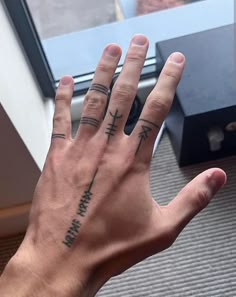 a person's hand with two tattoos on it, and the other hand is in front of a window