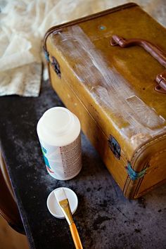 an old suitcase sitting on top of a table next to a paintbrush and cup