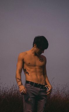 a shirtless man standing in the middle of a field with his hands on his hips