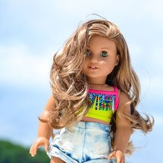 a close up of a doll with blonde hair and blue jeans shorts on the beach