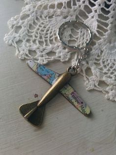 a fish shaped keychain with a map on it's side sitting on a lace doily