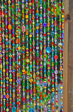 colorful beads are hanging on the side of a wooden structure in front of a tree