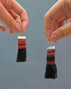 two hands holding small black and red tasseled earrings