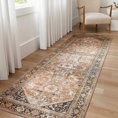 a large area rug in front of a window with white drapes on the windowsill