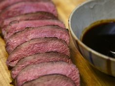 slices of beef on a wooden cutting board next to a bowl of bbq sauce