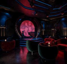 a dimly lit room with red and blue lighting on the walls, two round couches in front of a circular window