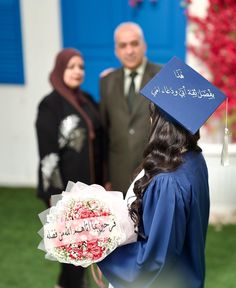 a woman wearing a graduation cap and gown holds flowers in front of an older man