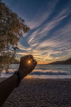 a person is holding their hand up to the sun at the beach with waves in the background