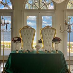 two white chairs sitting on top of a green table in front of large glass windows