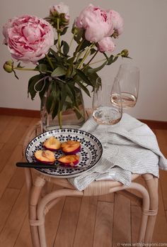 a plate with peaches on it next to a glass of wine and flowers in a vase