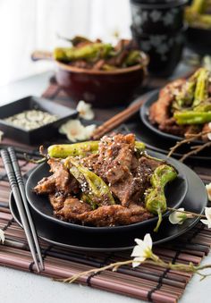 two black plates filled with food on top of a bamboo place mat next to chopsticks