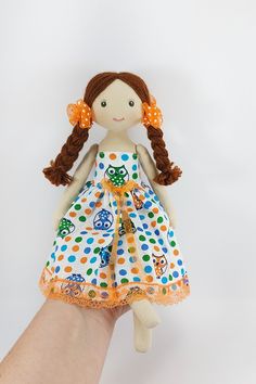 a hand is holding a doll with brown hair and polka dots on it's dress