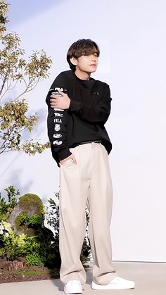 a young man standing in front of a white wall with his arms crossed and looking off to the side