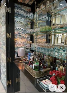 a bar with lots of bottles and glasses on top of the counter next to a vase filled with flowers