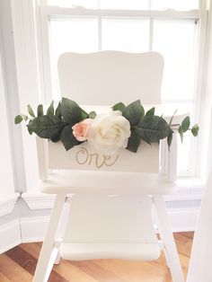 a white chair with flowers on it in front of a window and another chair behind it