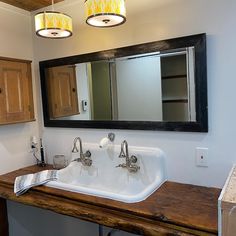 a bathroom sink sitting under a mirror next to a wooden counter with two lights on it