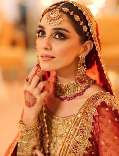 a woman in a red and gold bridal outfit poses for the camera with her hands on her chin