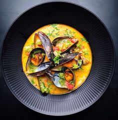 a black plate topped with mussels and broccoli