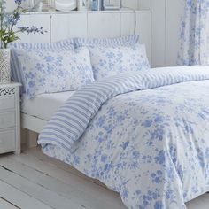 a white bed with blue flowers on the comforter and pillows in front of it