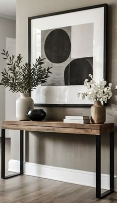 a wooden table with vases and flowers on it in front of a framed art piece