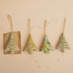 three small christmas trees are hanging from twine strings on the wall next to each other