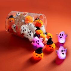 several halloween decorations in a plastic container on an orange surface, including pom - poms and ghost faces