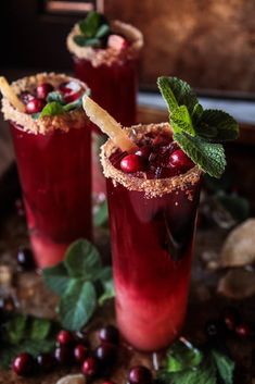 two glasses filled with cranberry shrub cocktails on top of leaves and berries