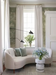 a white couch sitting in front of a window next to a vase filled with flowers