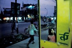 people are walking on the sidewalk at night in front of a yellow bus with its door open