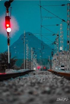 an empty train track at night with red lights on it and mountains in the background