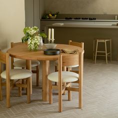 a wooden table with four chairs and a vase on top of it in front of a kitchen counter