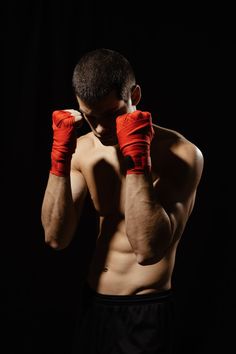 a shirtless man with red boxing gloves on his head and hands over his face