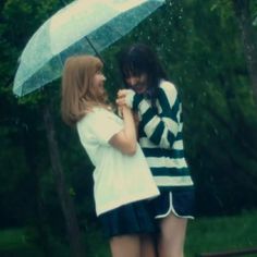 two young women standing under an umbrella in the rain, one holding her hand on another woman's shoulder