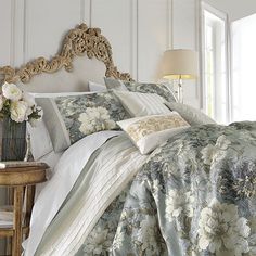 a bed with floral comforter and pillows in a white room next to a window