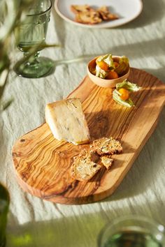 a wooden cutting board topped with food on top of a table next to wine glasses