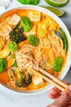 someone holding chopsticks over a bowl of soup with tofu and broccoli