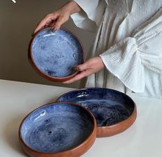 a woman holding two blue bowls on top of a white table next to another bowl