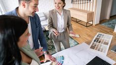 three people standing around a table with some paint samples on it and one person pointing to the floor plan