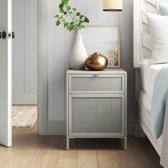 a bedroom with white walls and wood flooring has a gold vase on the nightstand