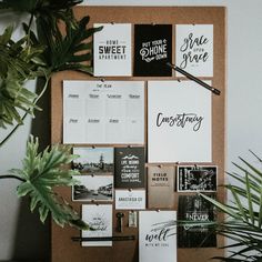 a cork board with several different types of cards on it next to a potted plant