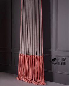 an orange and grey curtain hanging from the side of a wall in a room with gray walls