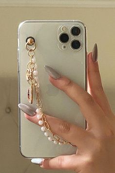 a woman's hand holding an iphone case with pearls and charms attached to it