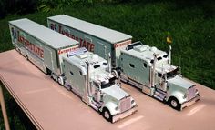 two toy semi trucks are sitting on a pink table in front of some green grass