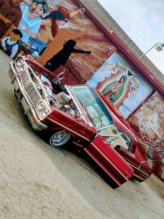 a red car parked in front of a wall with pictures on it's side