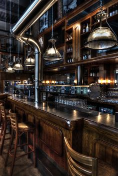 an empty bar with wooden stools and hanging lights