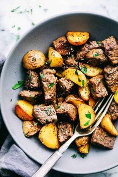 a bowl filled with meat and potatoes on top of a marble table next to a fork