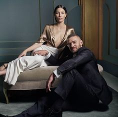 a man and woman sitting on a couch in front of a blue wall, posing for the camera