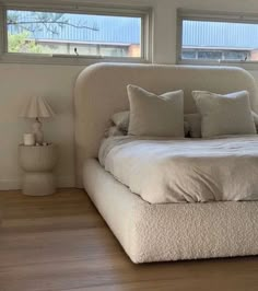 a white bed sitting in the middle of a bedroom next to two lamps and windows