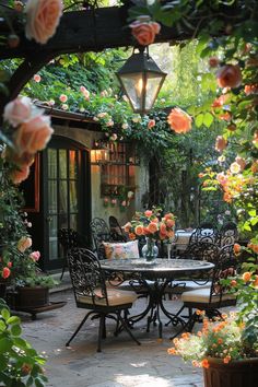 an outdoor dining table surrounded by flowers and potted plants with hanging lights in the background