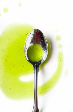 a spoon filled with green liquid on top of a white surface